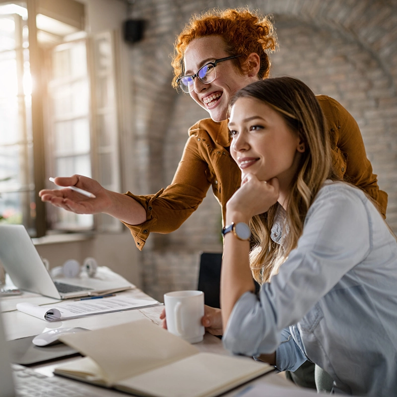 Happy female entrepreneurs reading an e-mail on computer while working together in the office. Focus is on redhead woman